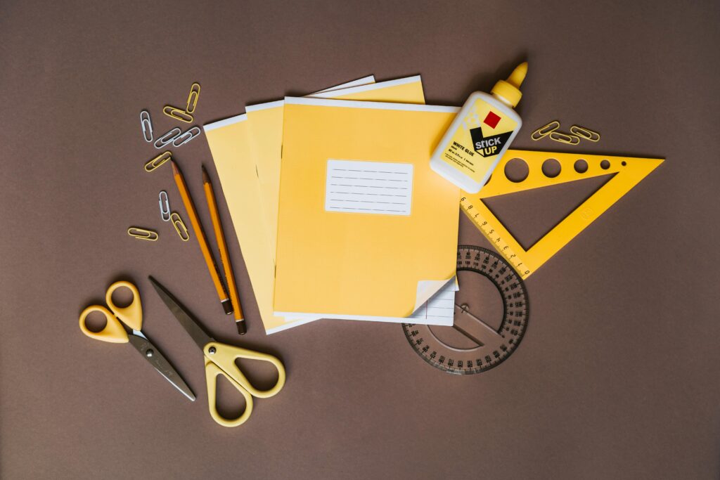 A flat lay of yellow stationery tools like pencils, scissors, and glue on a brown surface.